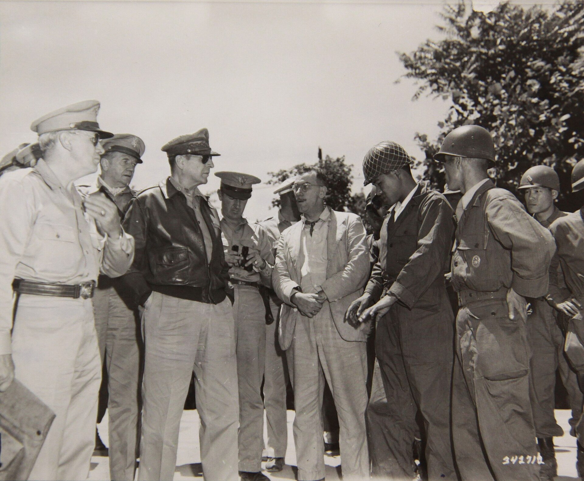 Douglas MacArthur stands outdoors among American staff and Korean officers during a close discussion of the invasion.