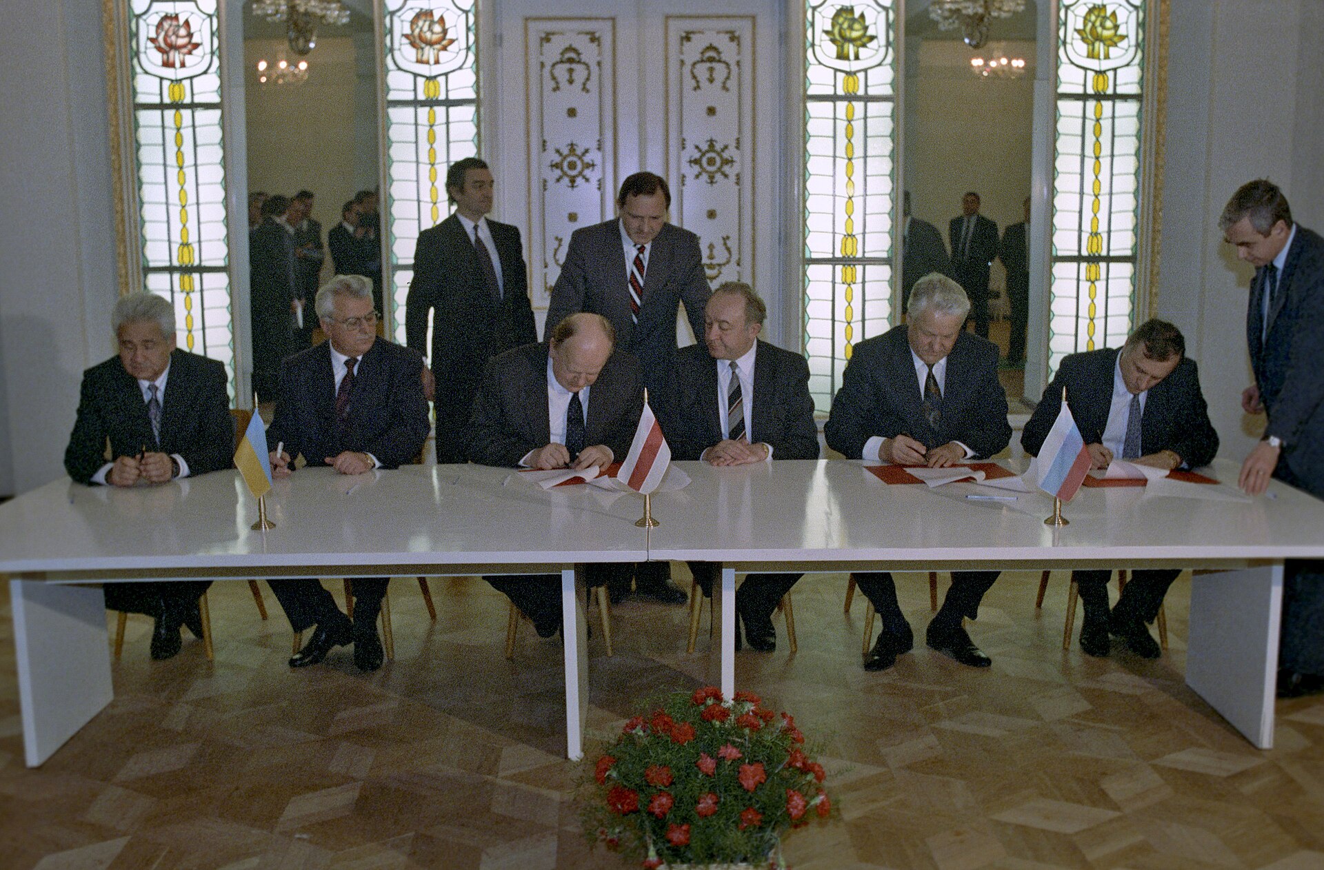 Leonid Kravchuk and Stanislav Shushkevich sit signing documents as Boris Yeltsin watches across the table.
