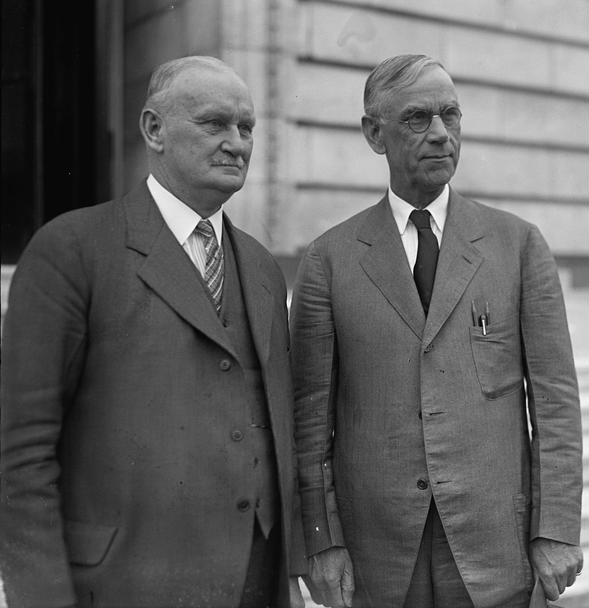 Senator Reed Smoot and Representative Willis Hawley stand together outside a government building in Washington.