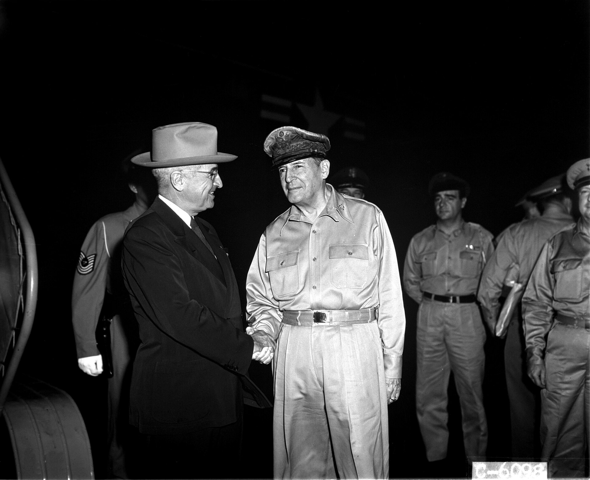 President Harry Truman and General Douglas MacArthur shake hands outdoors during their Wake Island meeting.