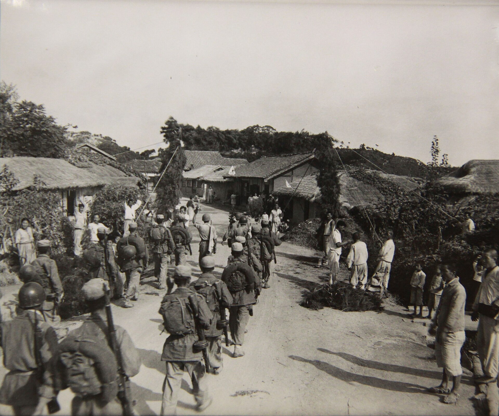 Villagers raise a welcome arch over a road as Republic of Korea troops pass northward beneath it.
