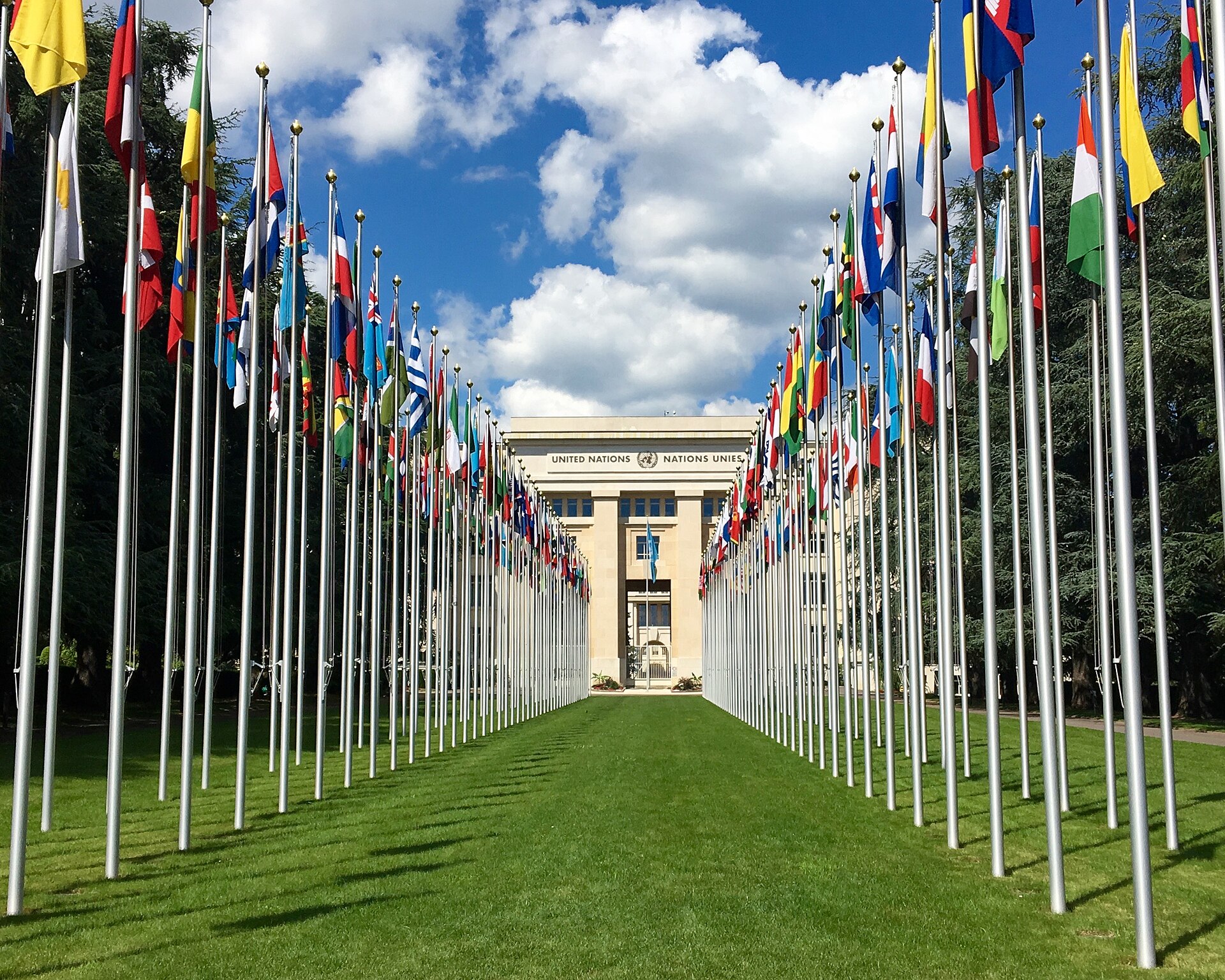 Rows of national flags lead toward the Palace of Nations in Geneva.