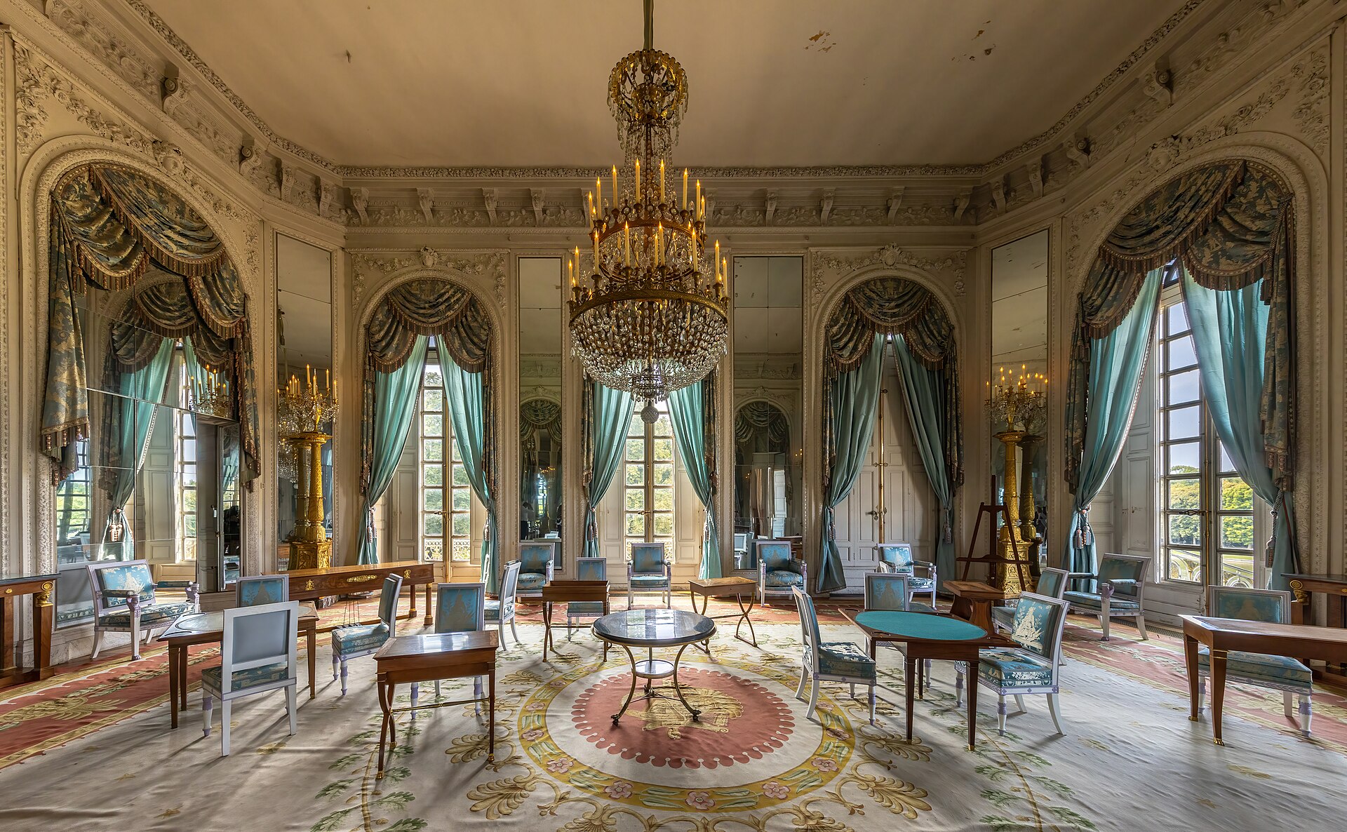 A mirrored salon in the Grand Trianon with a chandelier, pale panelling and tall windows onto the gardens.