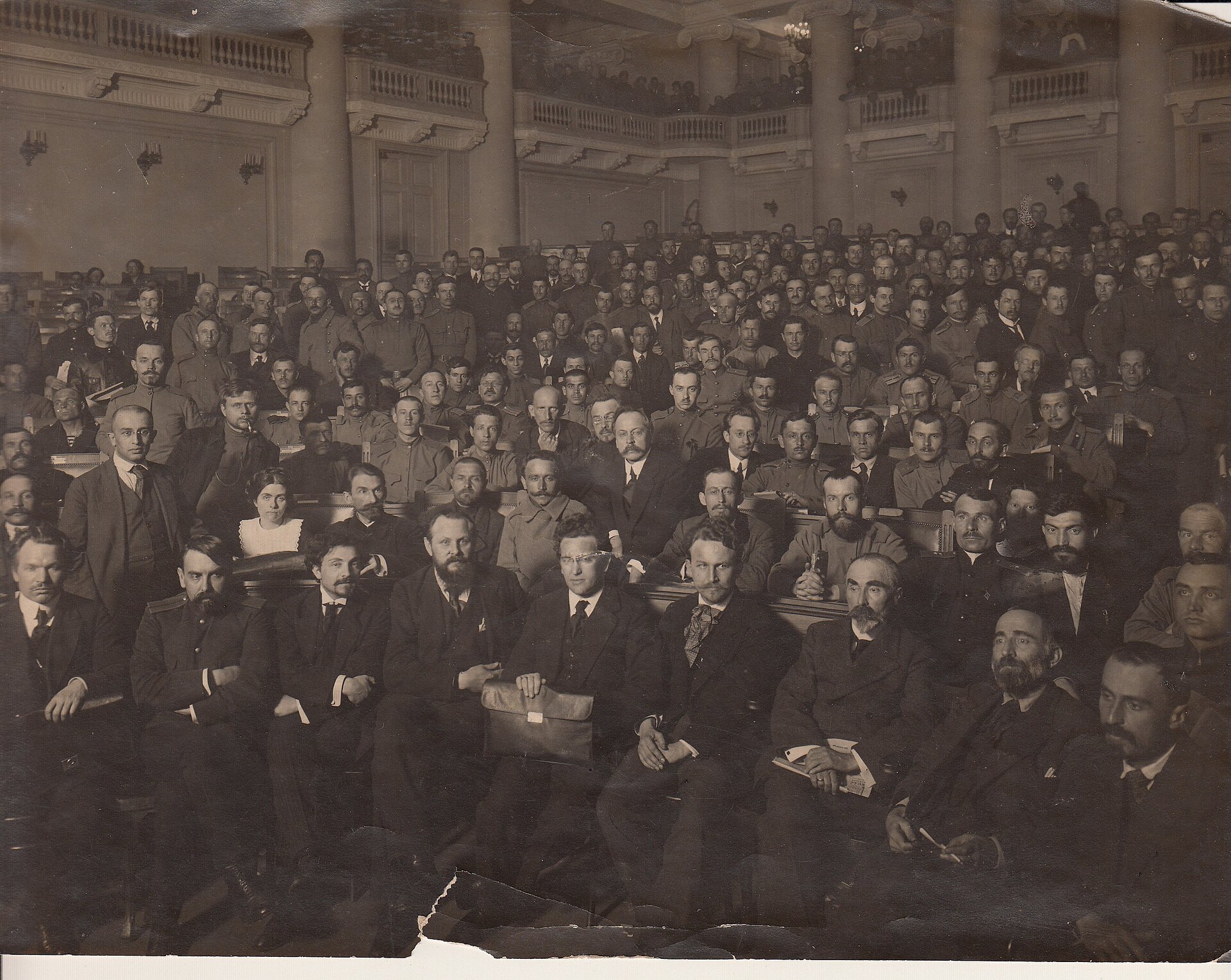 Members of the Petrograd Soviet pose together in several rows inside a large meeting hall in 1917.