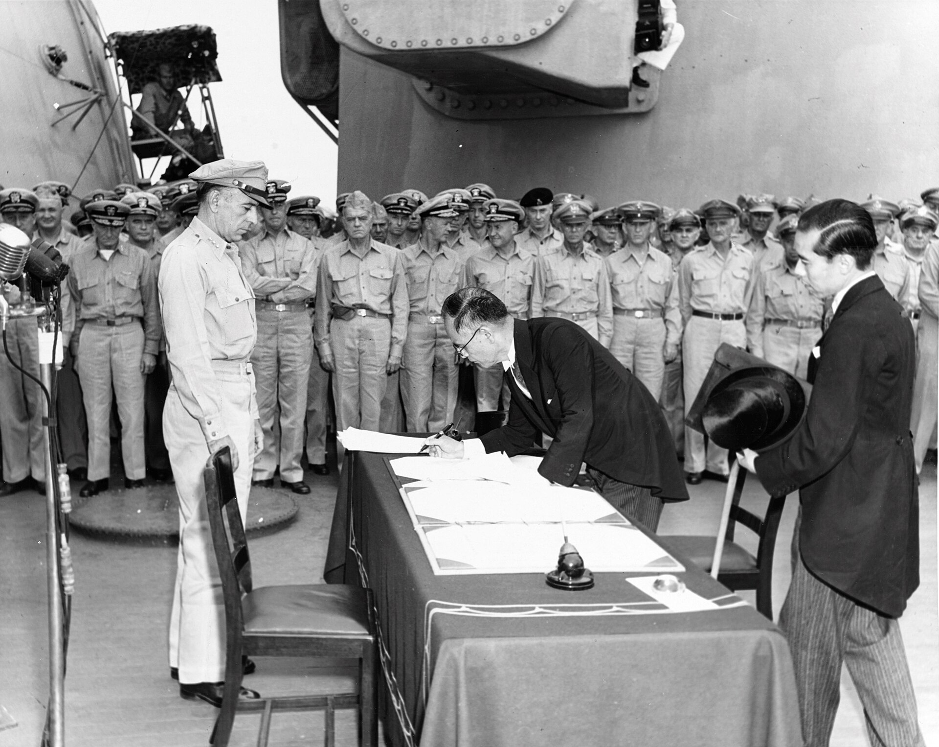 Mamoru Shigemitsu signs a document aboard USS Missouri while Allied representatives watch.