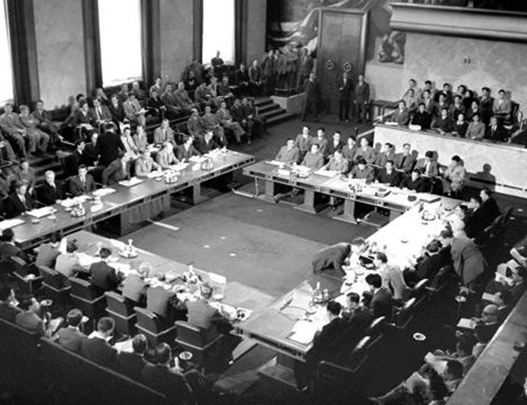 Delegates sit around a large conference table during the 1954 Geneva negotiations on Indochina and Korea.