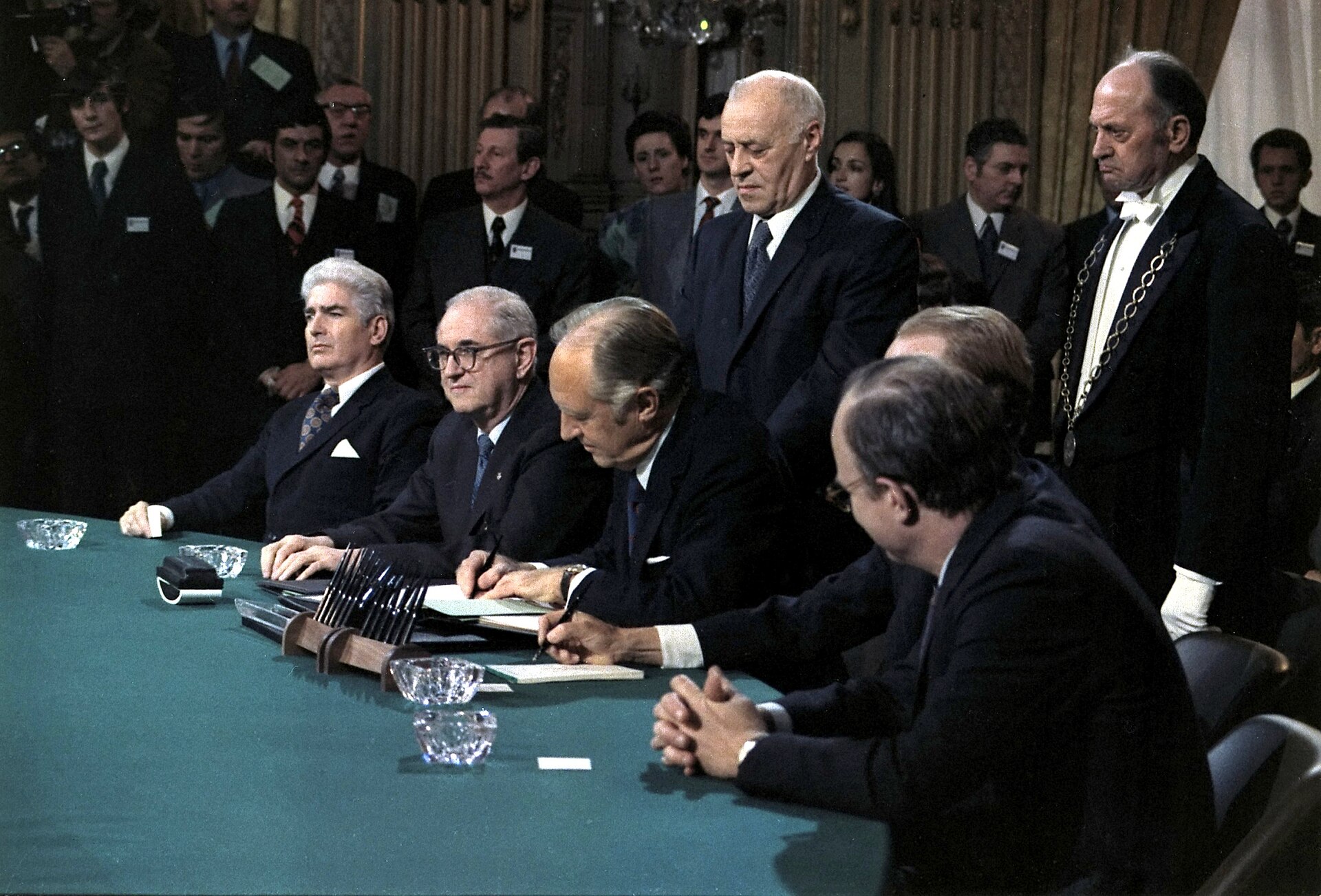 Four delegations seated at a conference table sign the agreement ending direct United States involvement in the Vietnam War.